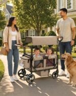 Parents strolling two kids in the brown stroller wagon on a sunny sidewalk, family walk with large 10-inch rear wheels